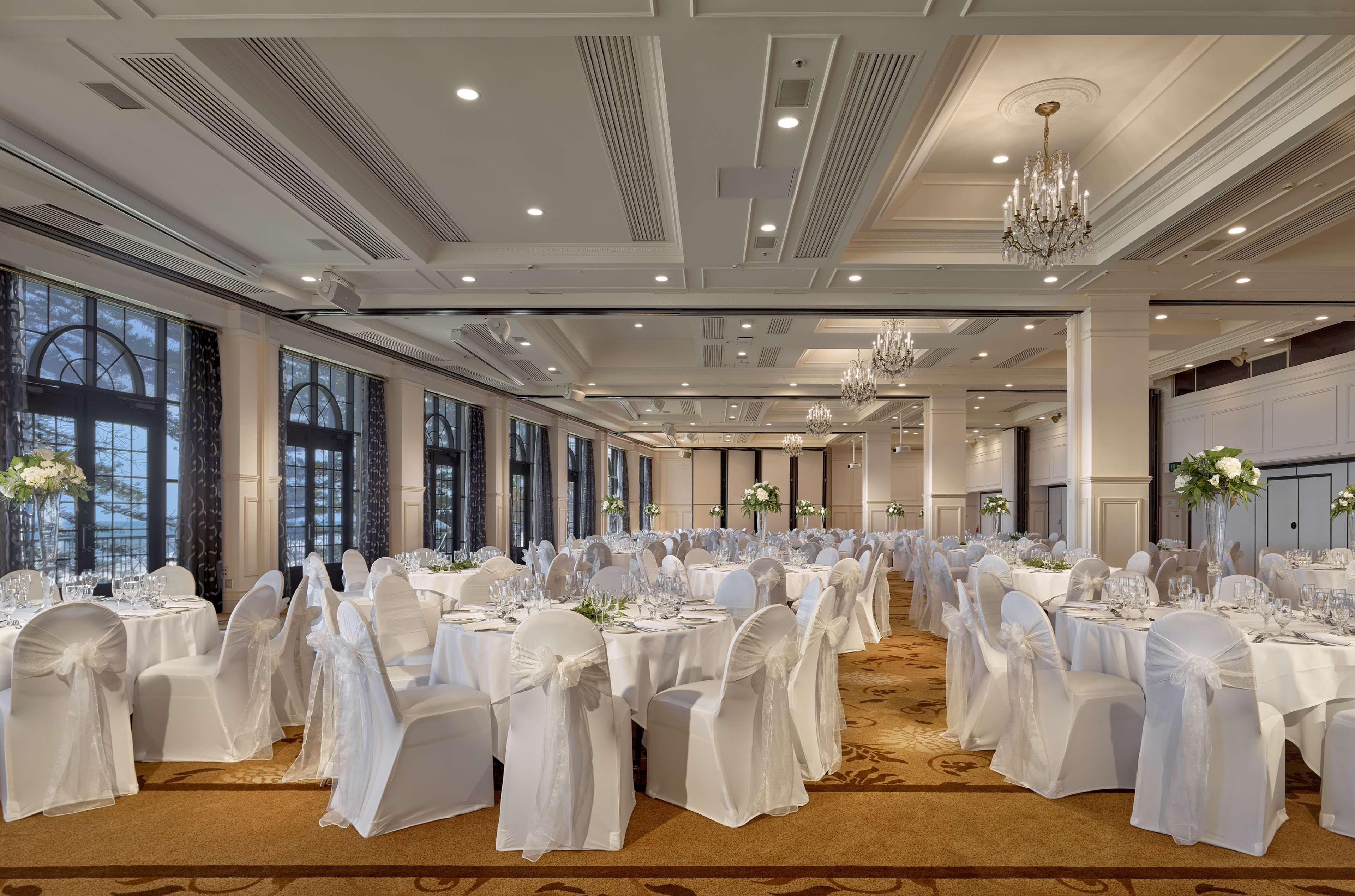 Hotel Stamford Grand Adelaide à Glenelg Extérieur photo The photo depicts an elegantly arranged banquet hall or dining area. The space features multiple round tables, each set with white tablecloths and decorated with floral centerpieces. The chairs are covered in white fabric, contributing to a formal at