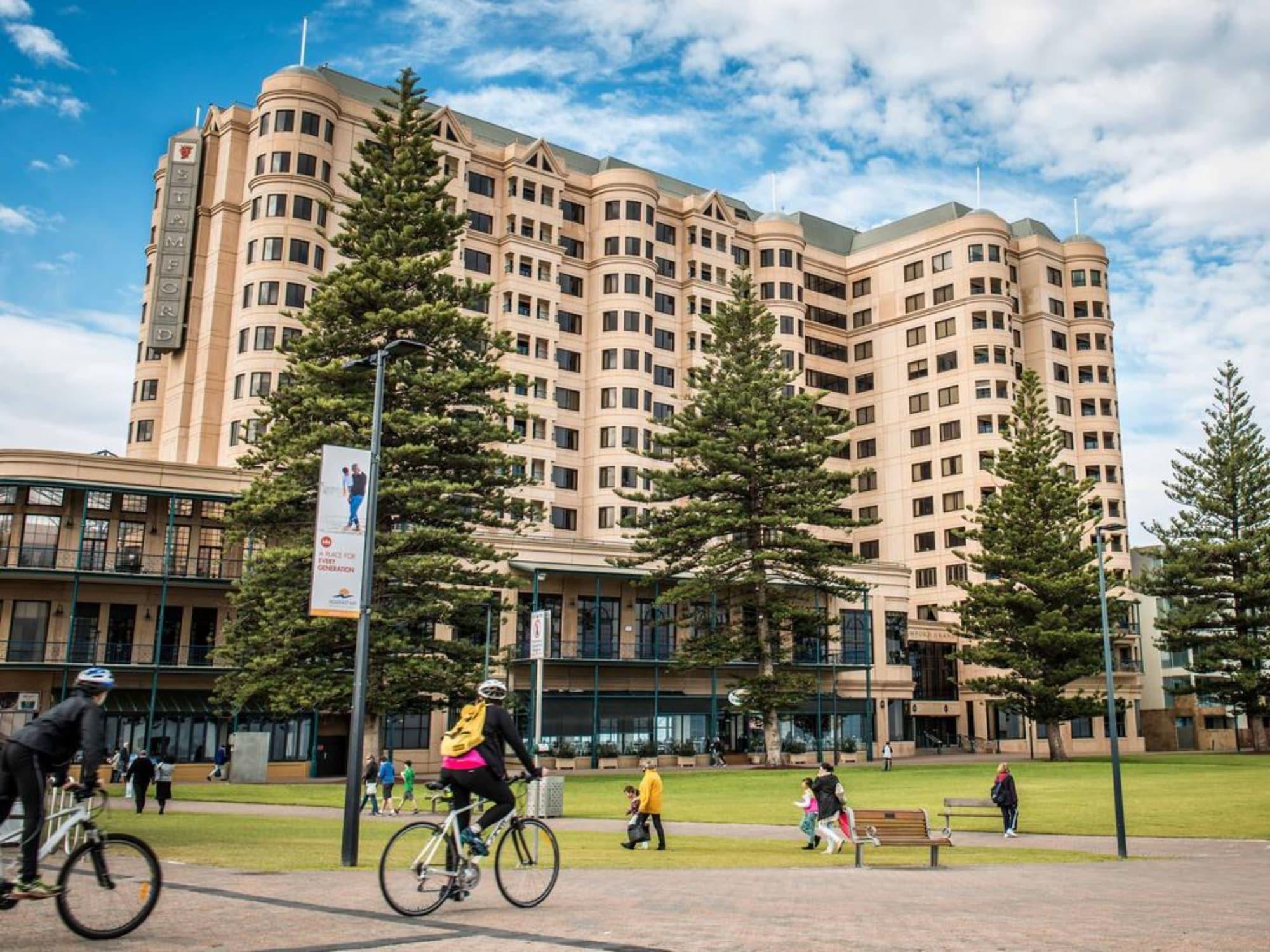 Hotel Stamford Grand Adelaide à Glenelg Extérieur photo The photo depicts a modern building with a large facade, likely a hotel or commercial establishment, situated near a spacious green area. Surrounding the building are several tall trees, providing shade and enhancing the aesthetic appeal. In the fore