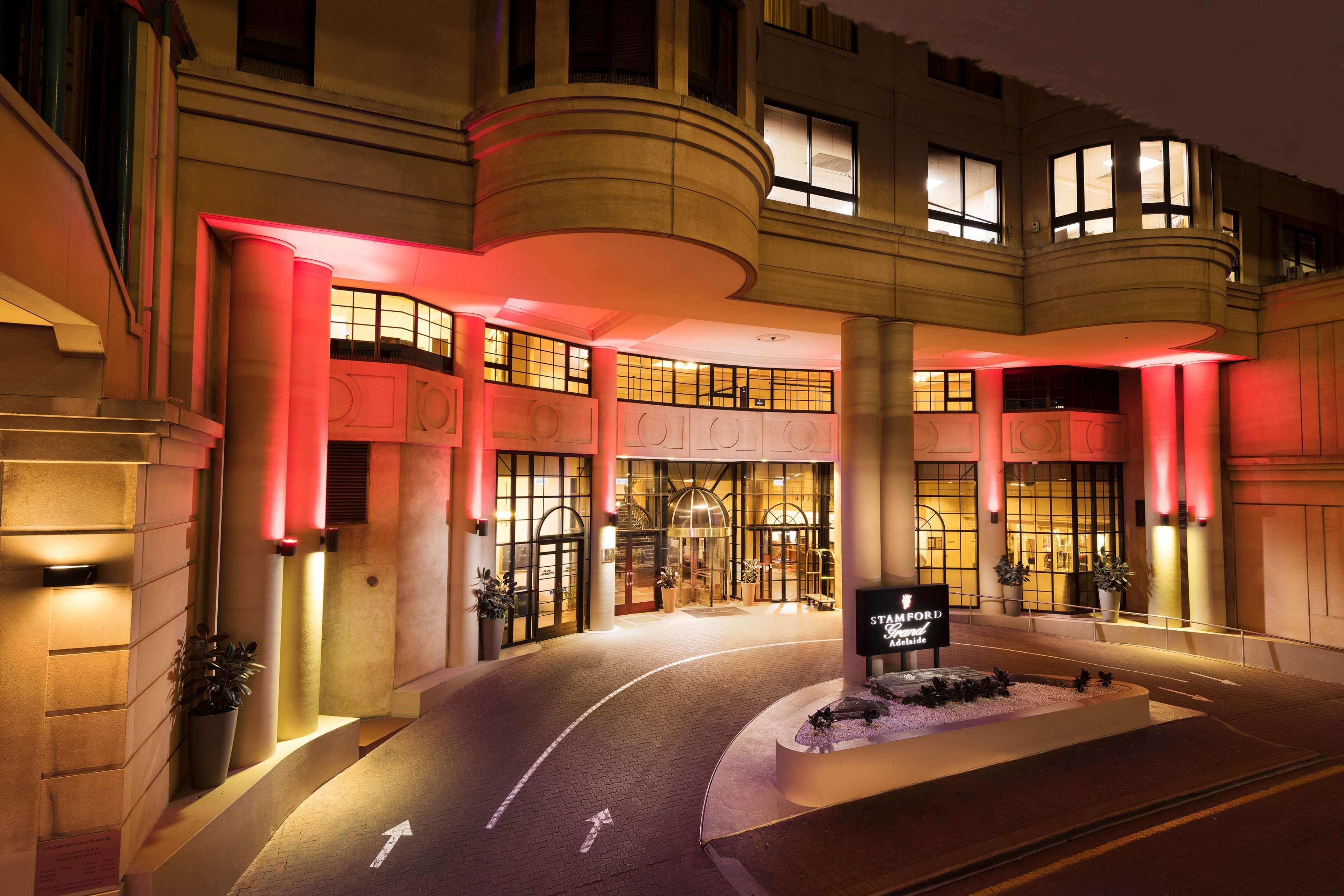 Hotel Stamford Grand Adelaide à Glenelg Extérieur photo The photo shows the entrance of a hotel or luxury building at night. The façade features a modern architectural style with large windows and an elegant entrance. The area is illuminated with red lighting, creating an inviting atmosphere. There appear