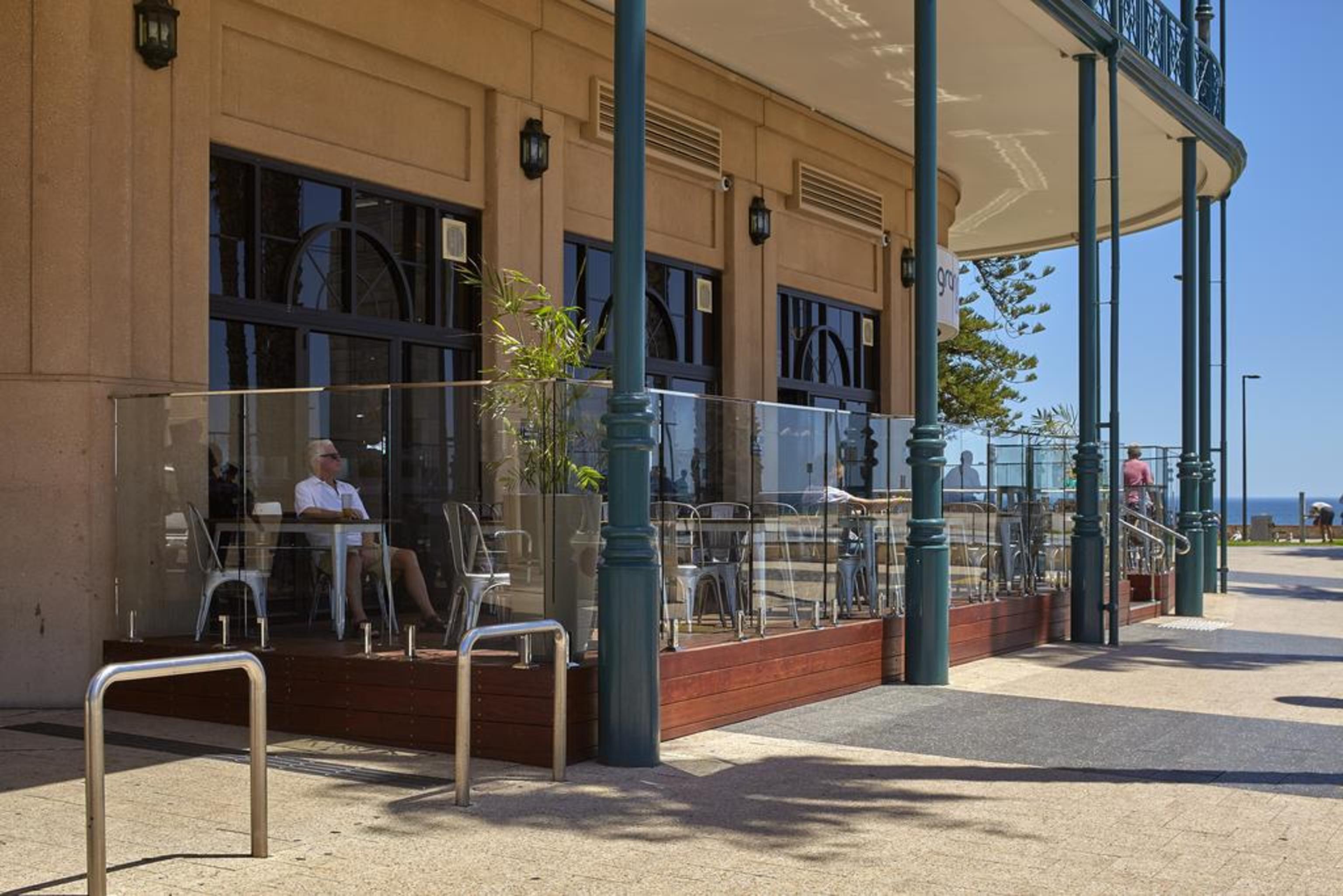 Hotel Stamford Grand Adelaide à Glenelg Extérieur photo The photo shows the exterior of a cafe or restaurant with a large outdoor seating area. There are glass barriers around the seating, providing a view of the outside while maintaining a sense of enclosure. The building has a modern architectural style
