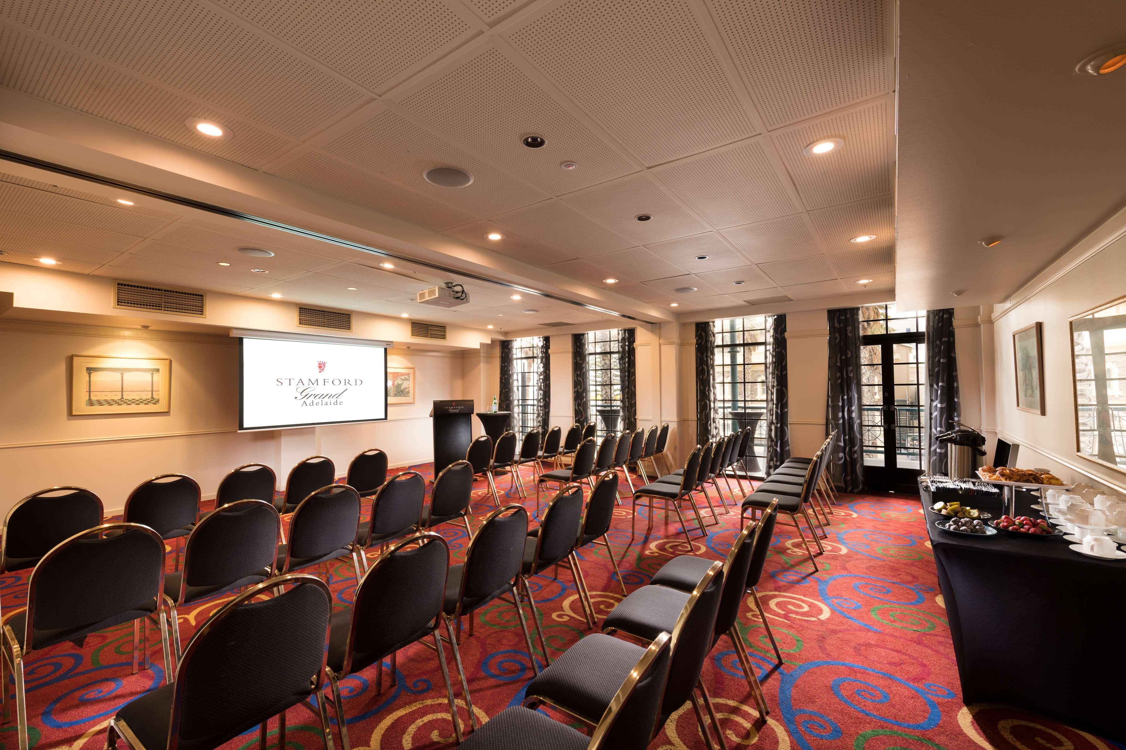 Hotel Stamford Grand Adelaide à Glenelg Extérieur photo The photo shows a conference room set up for an event. There are rows of black chairs arranged in a semicircular formation facing a presentation screen at the front. The room features large windows that allow natural light to enter, and the flooring 