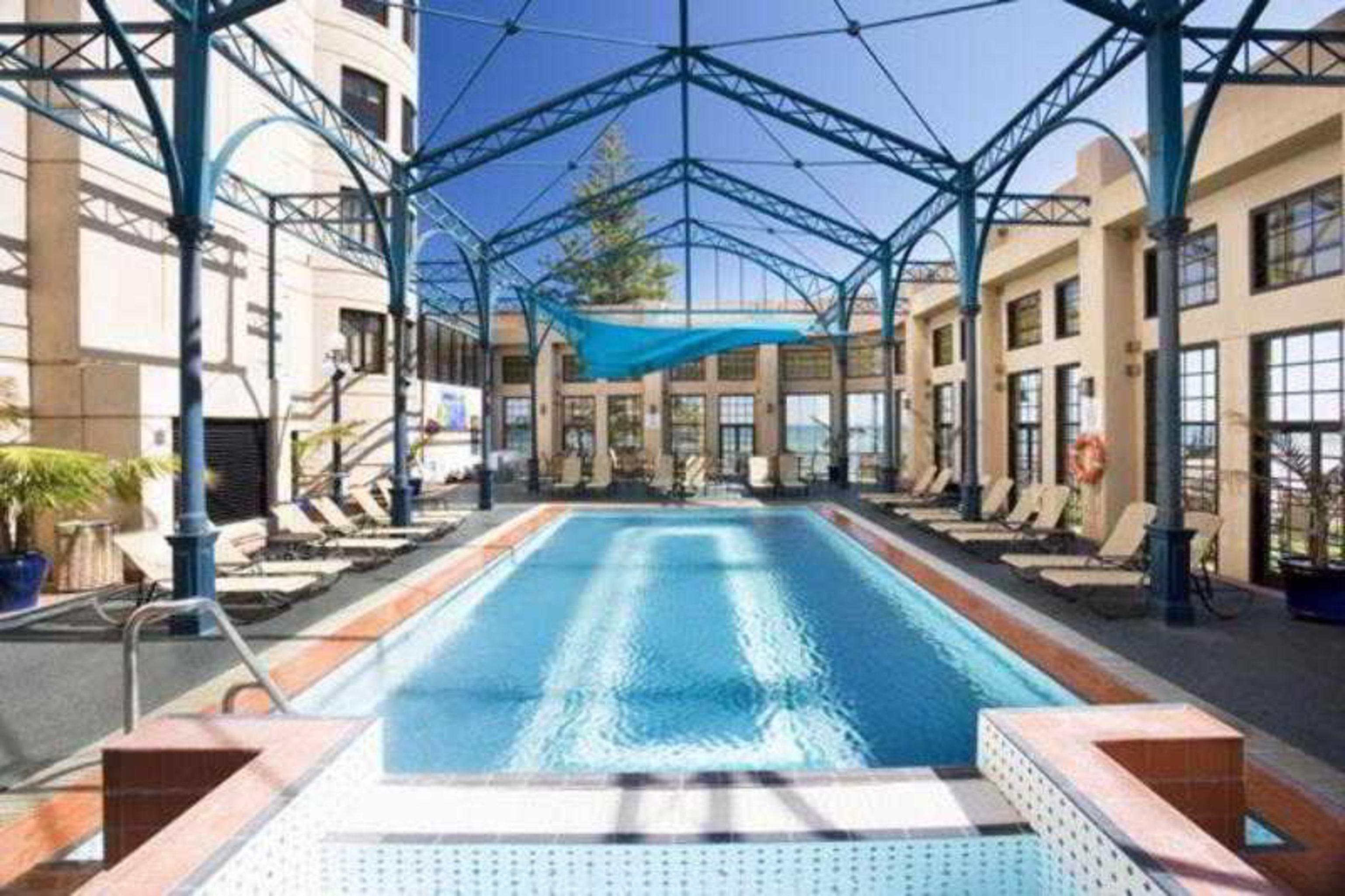 Hotel Stamford Grand Adelaide à Glenelg Facilités photo The photo shows an indoor swimming pool area. The pool is rectangular and features a blue cover above, supported by a metal frame. Surrounding the pool are several lounge chairs, and the space is well-lit with large windows allowing natural light to 
