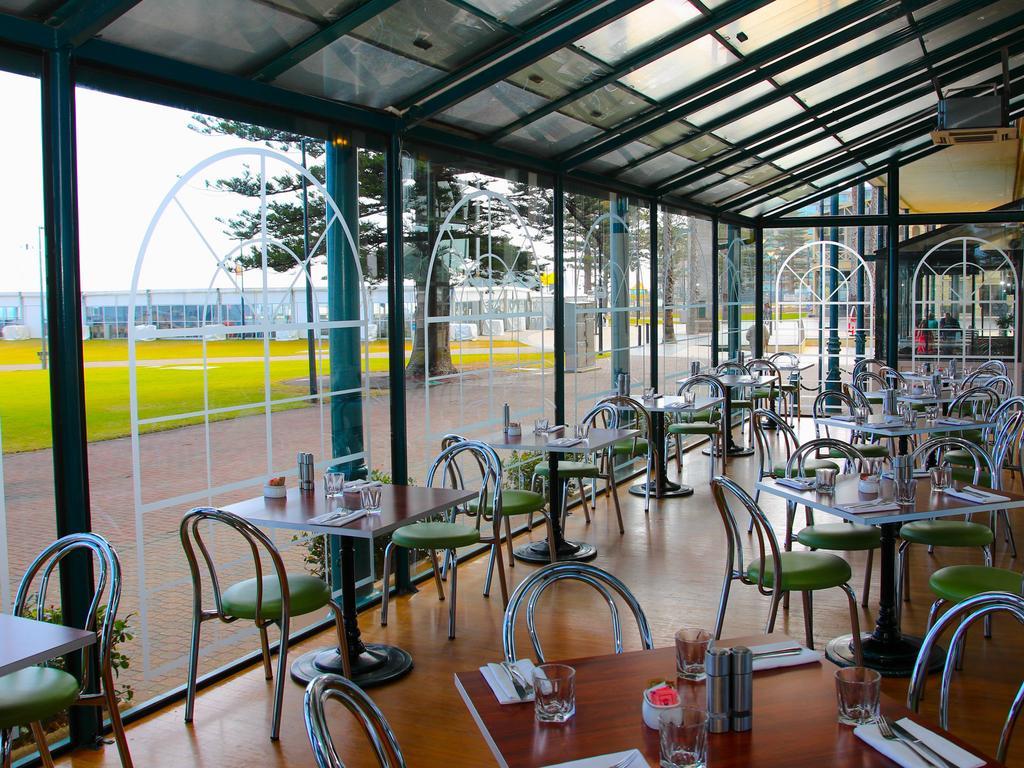 Hotel Stamford Grand Adelaide à Glenelg Extérieur photo The photo shows the interior of a restaurant with a modern design. The space features several tables with green chairs, arranged in a way that allows for ample seating. Large glass windows provide a view of the outside, creating a bright and open atm
