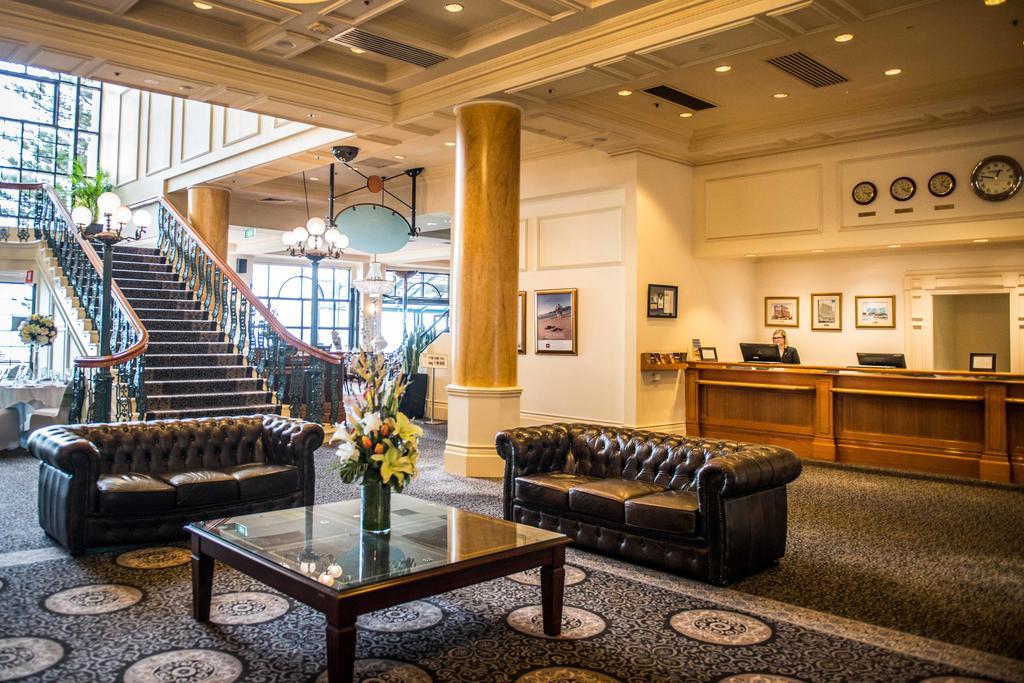 Hotel Stamford Grand Adelaide à Glenelg Extérieur photo The photo depicts a hotel lobby featuring a spacious and elegant design. There are two dark leather sofas arranged in front of a glass coffee table, adorned with a floral centerpiece. The lobby has a refined atmosphere, highlighted by large windows t