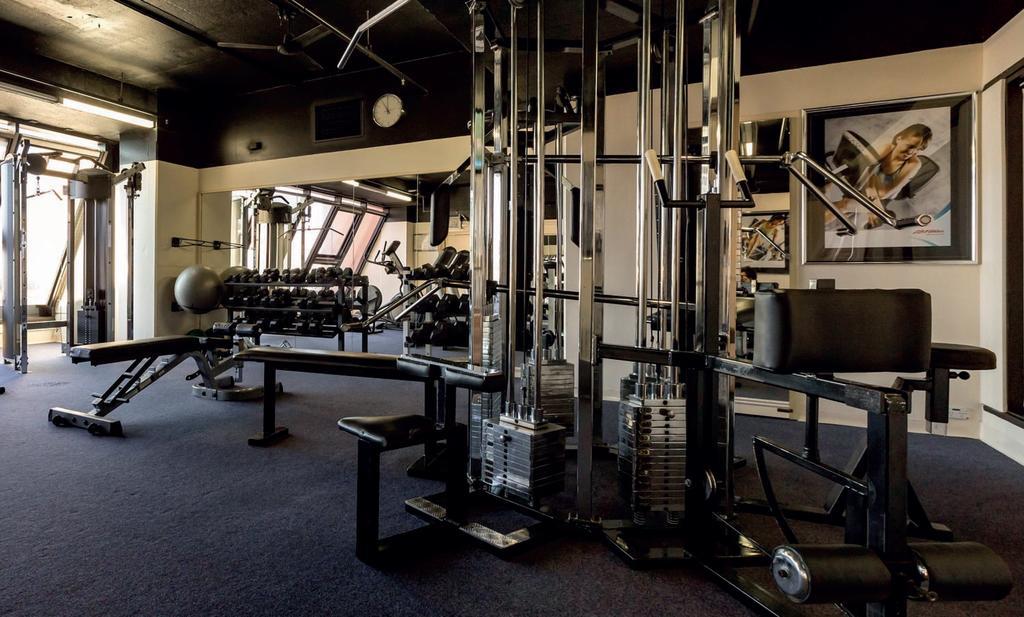 Hotel Stamford Grand Adelaide à Glenelg Extérieur photo The photo shows a gym interior with several pieces of exercise equipment. In the foreground, there is a multi-station machine that features various pulleys and weights. To the side, there are benches and free weights, including dumbbells. The gym has